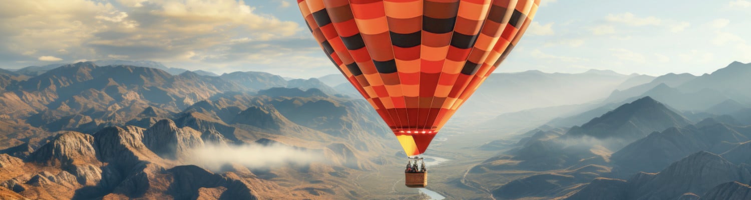 Farbiger Heißluft-Ballon schwebt über einem Tal zwischen schroffen Bergen.